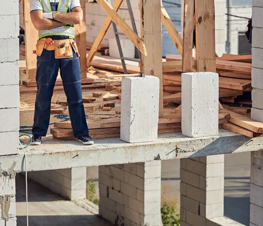 A man wearing a tool belt stands on a construction site, ready to work on the ongoing project.